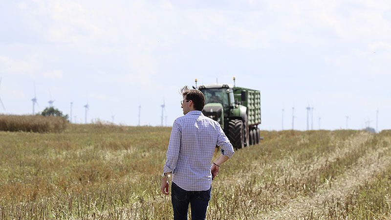 Landwirt Martin Niedzwetzki, WindBauer Geschäftsführer, auf dem Feld vor Traktor und Windenergieanlage.